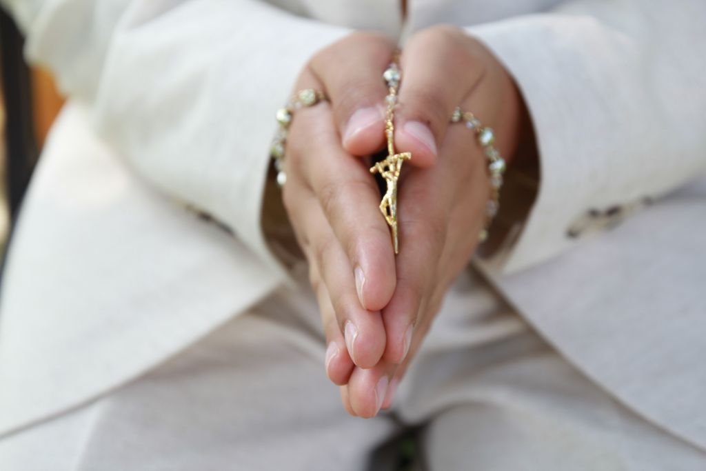 Close-up of hands in prayer holding a golden crucifix and rosary beads, symbolizing faith.