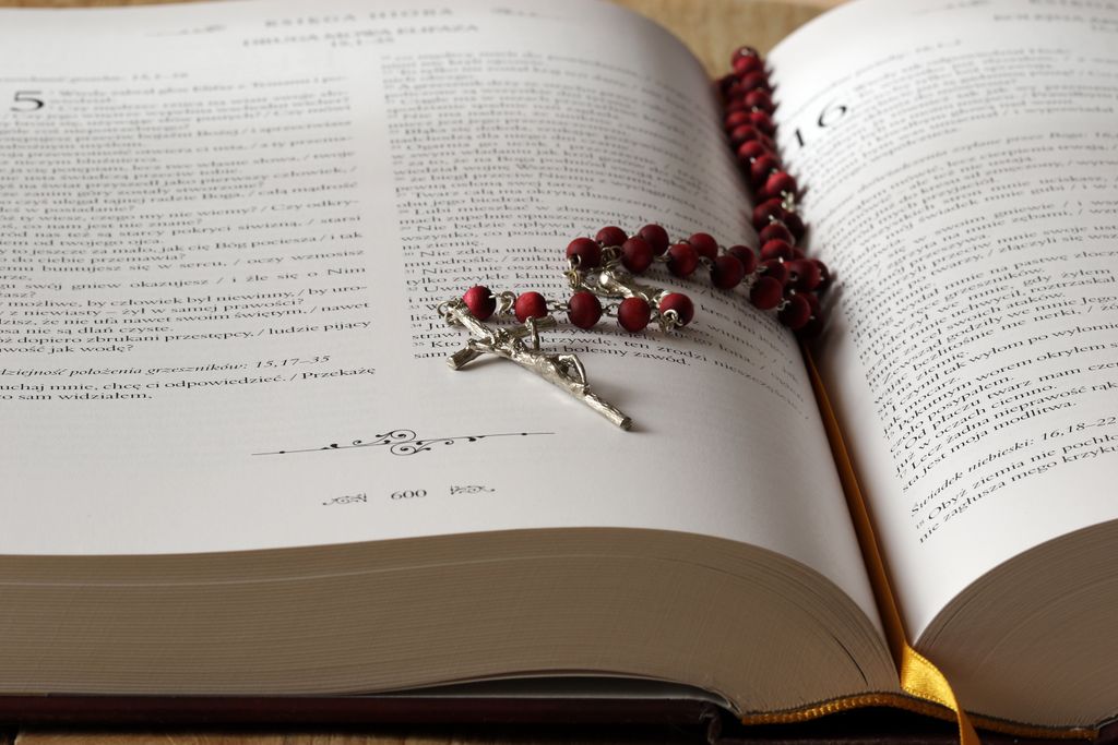 Open Bible with red rosary beads draped on pages, symbolizing faith and devotion.