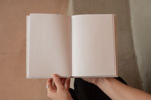 Unrecognizable female sitting and holding opened book with white blank pages on blurred background
